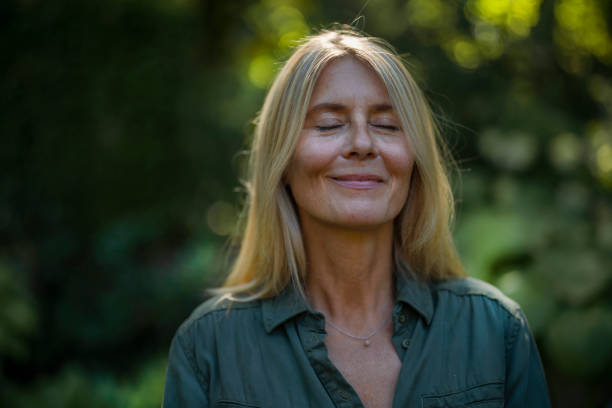 une femme de 50 ans dans la nature, reconnectée à elle-même, souriant à la vie, à l'écoute de ses ressentis