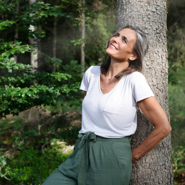 une femme de 50 ans adossée contre un arbre savourant sa sérénité retrouvée